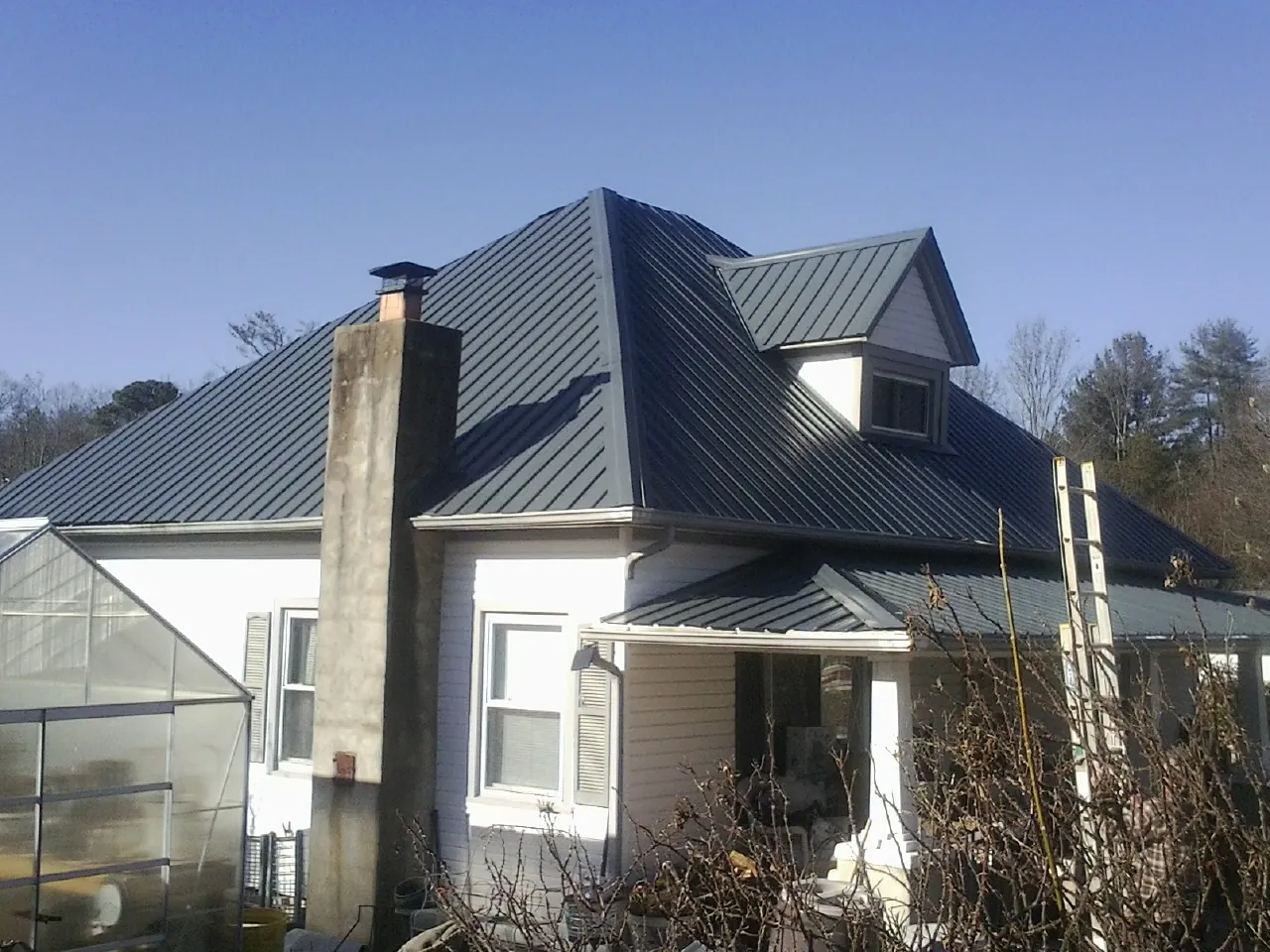 Dark blue standing seam metal roof on a white farmhouse with dormer — Slate & Tile Roof Repair by Roofing Brothers in Auburntown