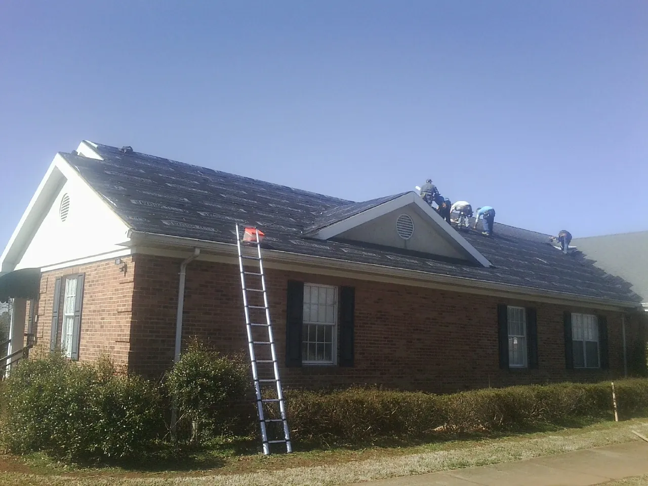 Crew tearing shingles off a brick ranch roof with a ladder set — Metal Roof Repair work by our crew in Auburntown