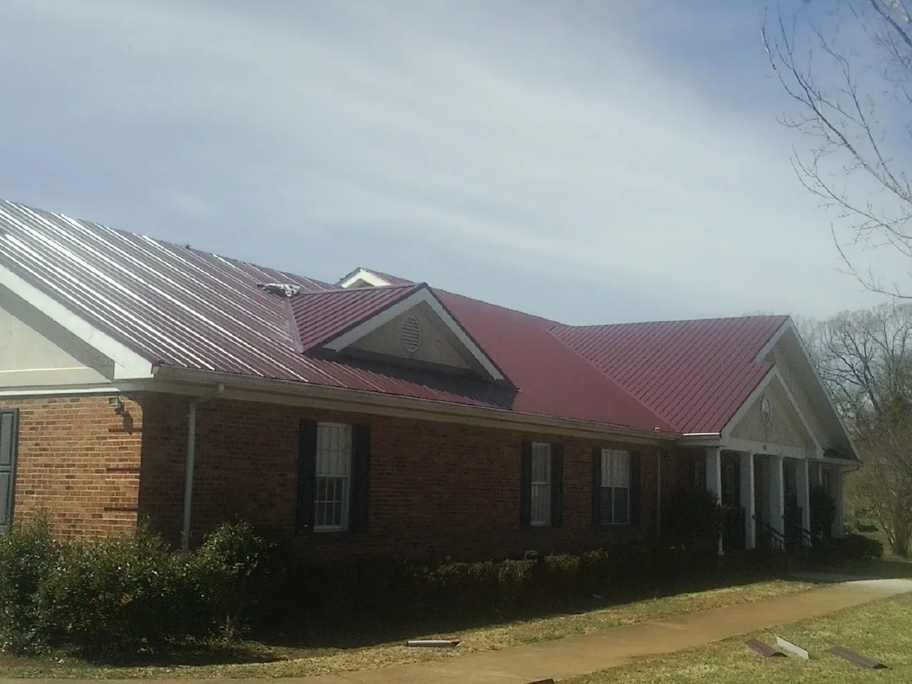 Red metal roof with gabled entries on a long brick building, from a Hail Damage Roof Repair job in Auburntown