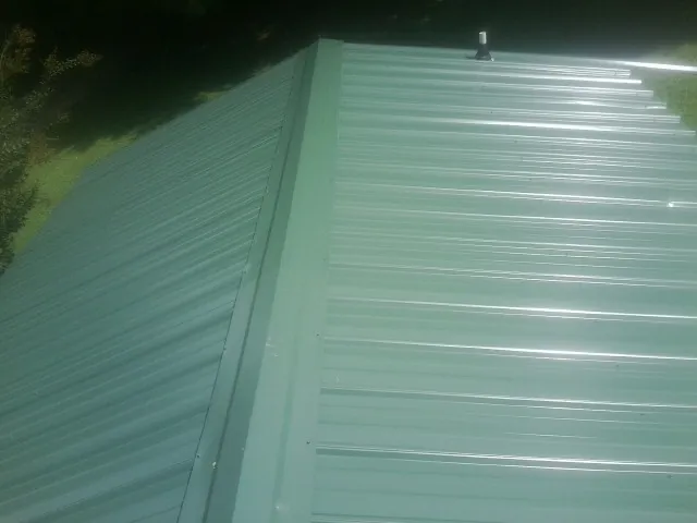 New green metal panels meeting at the ridge of a roof — Flat Roof Repair work by our crew in Auburntown