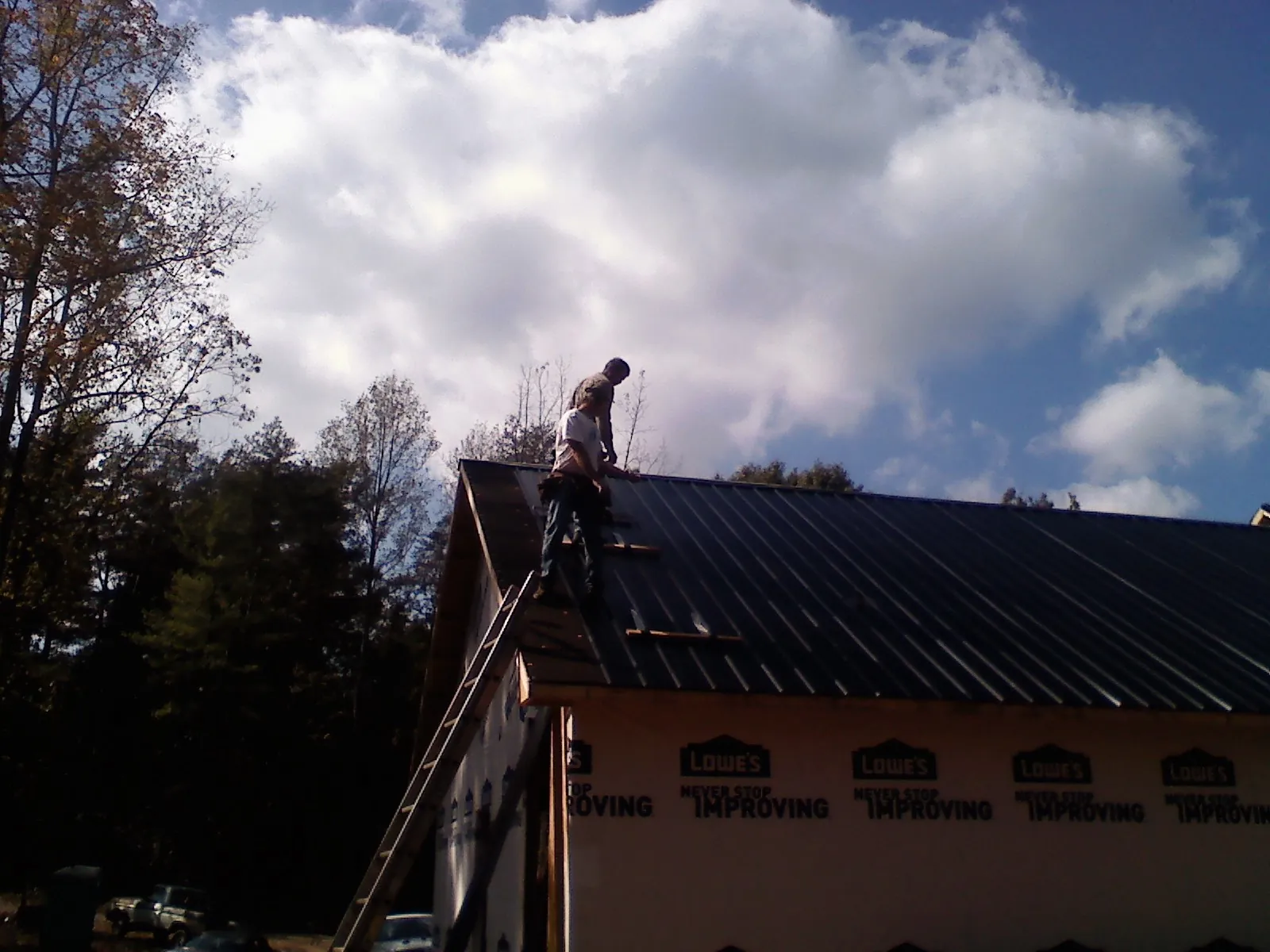 Roofer fastening dark metal panels high against a cloudy sky, from a Roof Inspection job in Auburntown