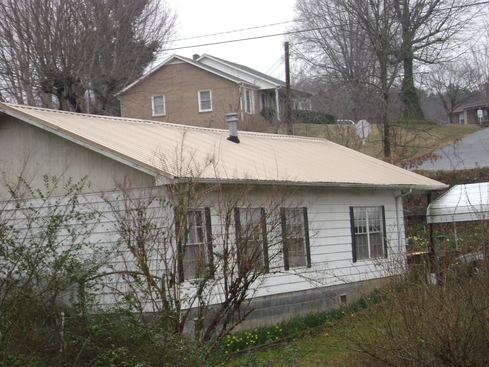 Tan metal roof on a white sided house set into a hillside — Commercial Roofing by Roofing Brothers in Auburntown