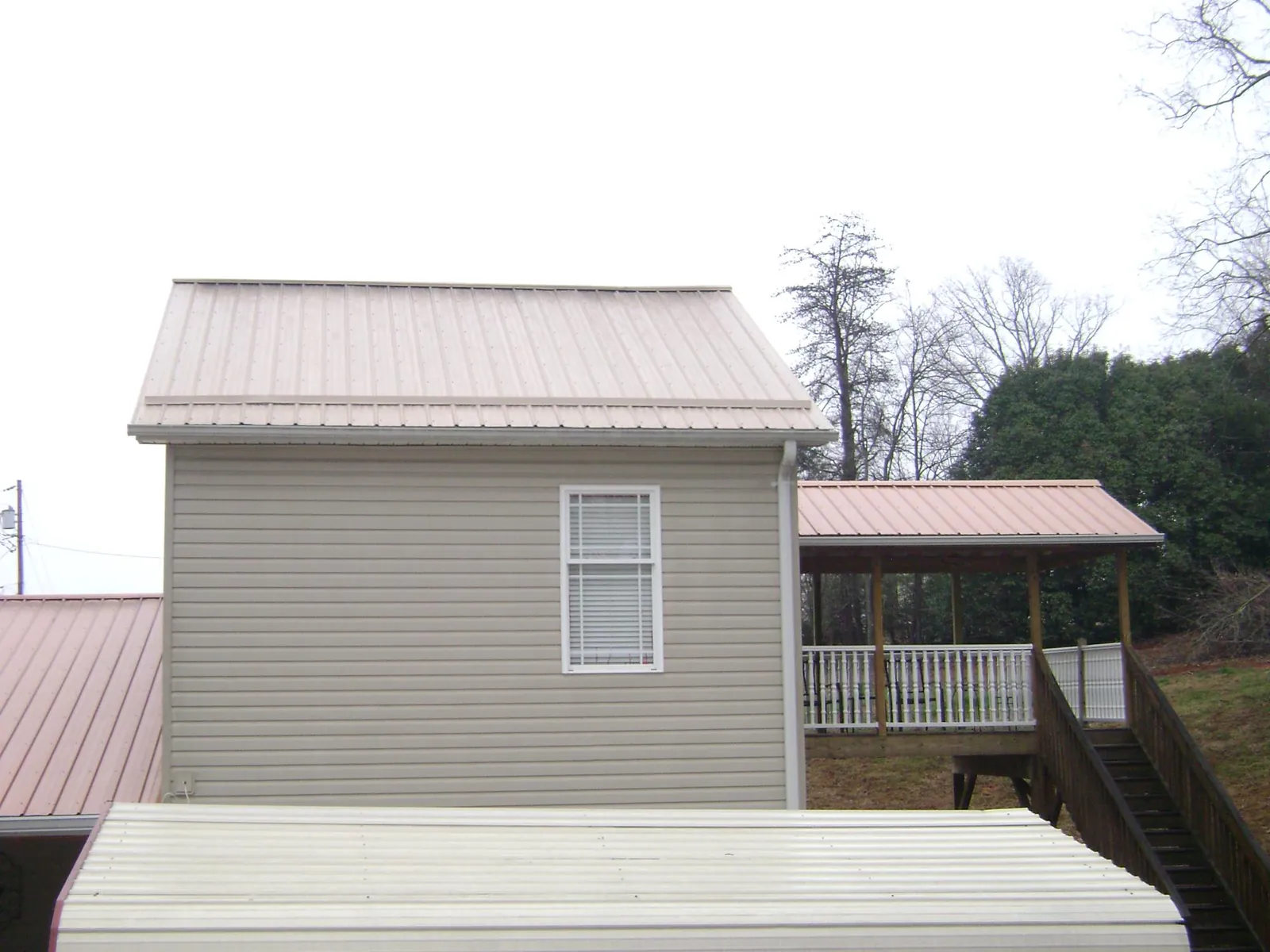 Tan metal roofs on a two story addition and attached porch, from a Roof Replacement job in Auburntown